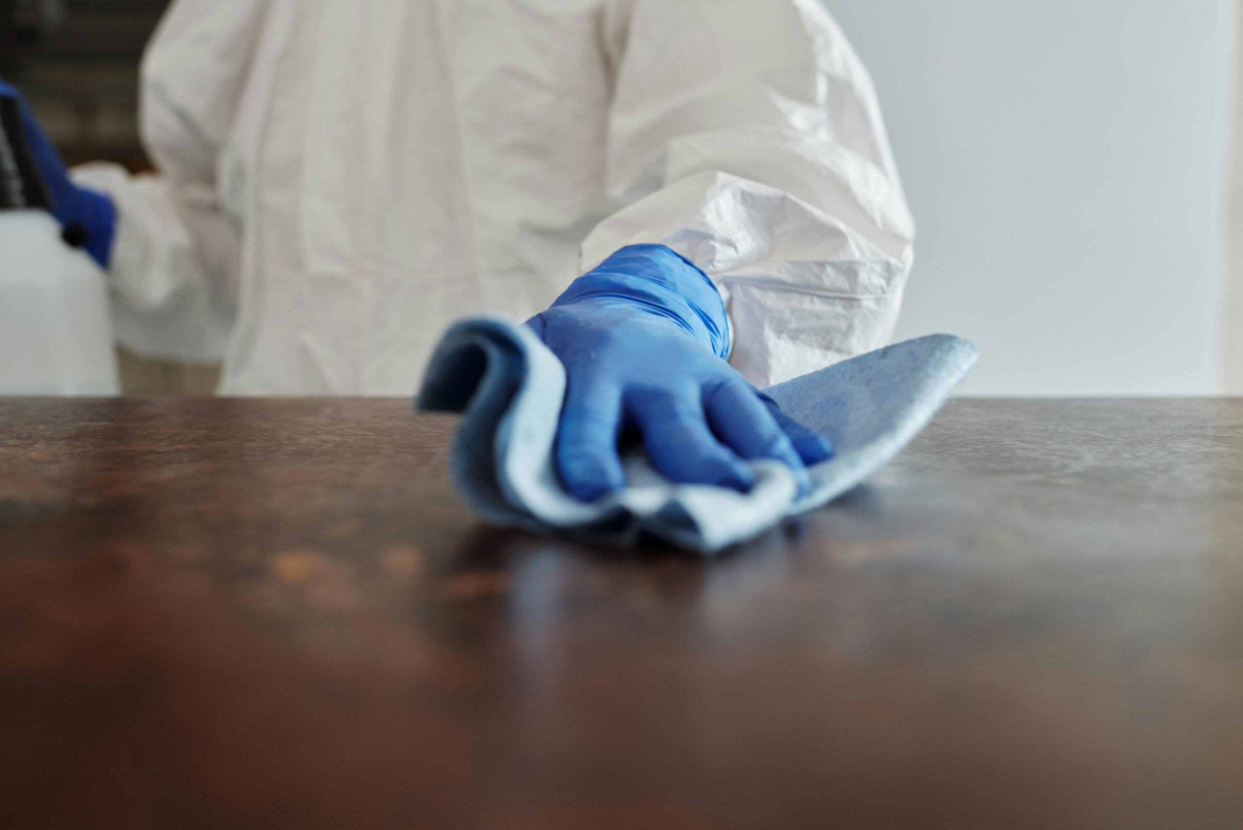 pexels-photo-4099467-4099467 Person in protective suit using disinfectant on surface to ensure cleanliness and safety.